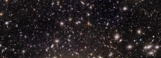 Image of the Perseus galaxy cluster with approximately a thousand galaxies in the foreground and more than a hundred thousand in the background. The galaxies are recognizable as smaller and larger points of light. Some also appear as spirals.